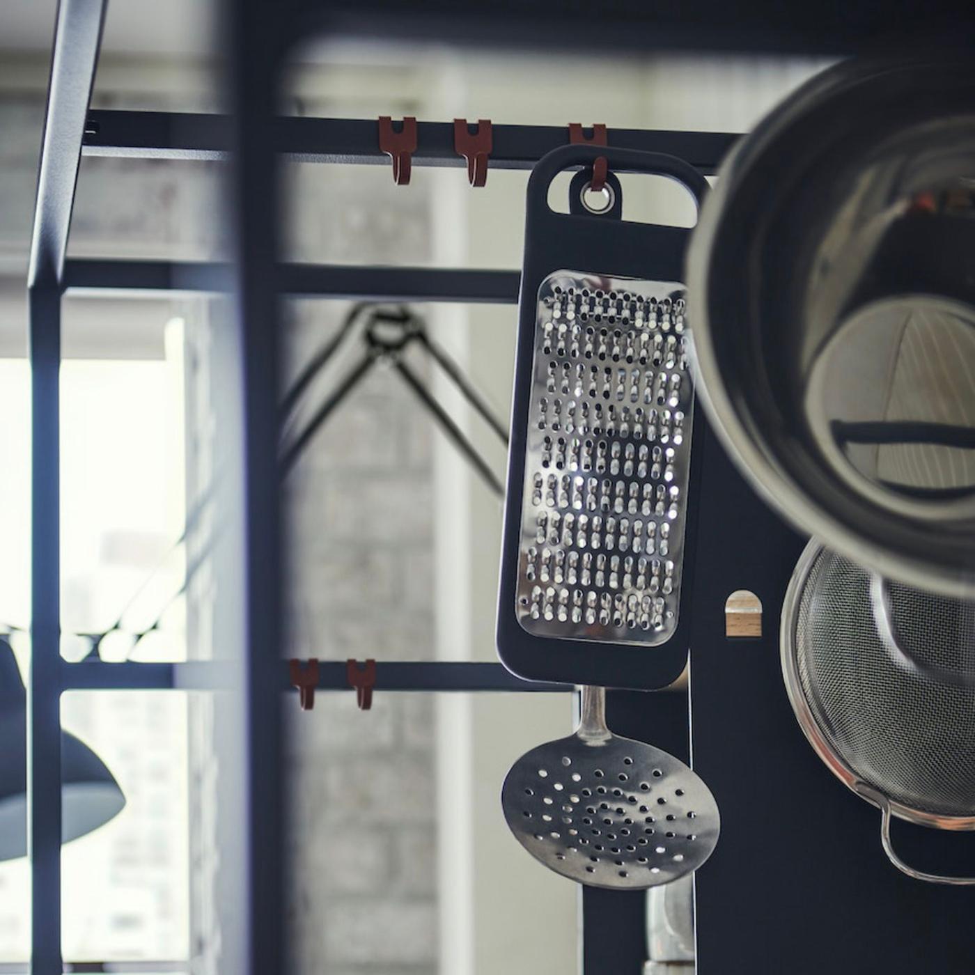 A grater and a slotted spoon hanging in a kitchen.