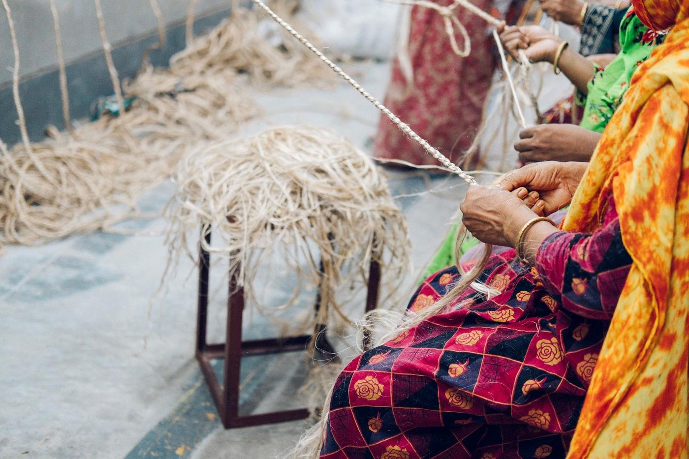 A person in colourful clothes sitting on a chair braiding natural fibres.