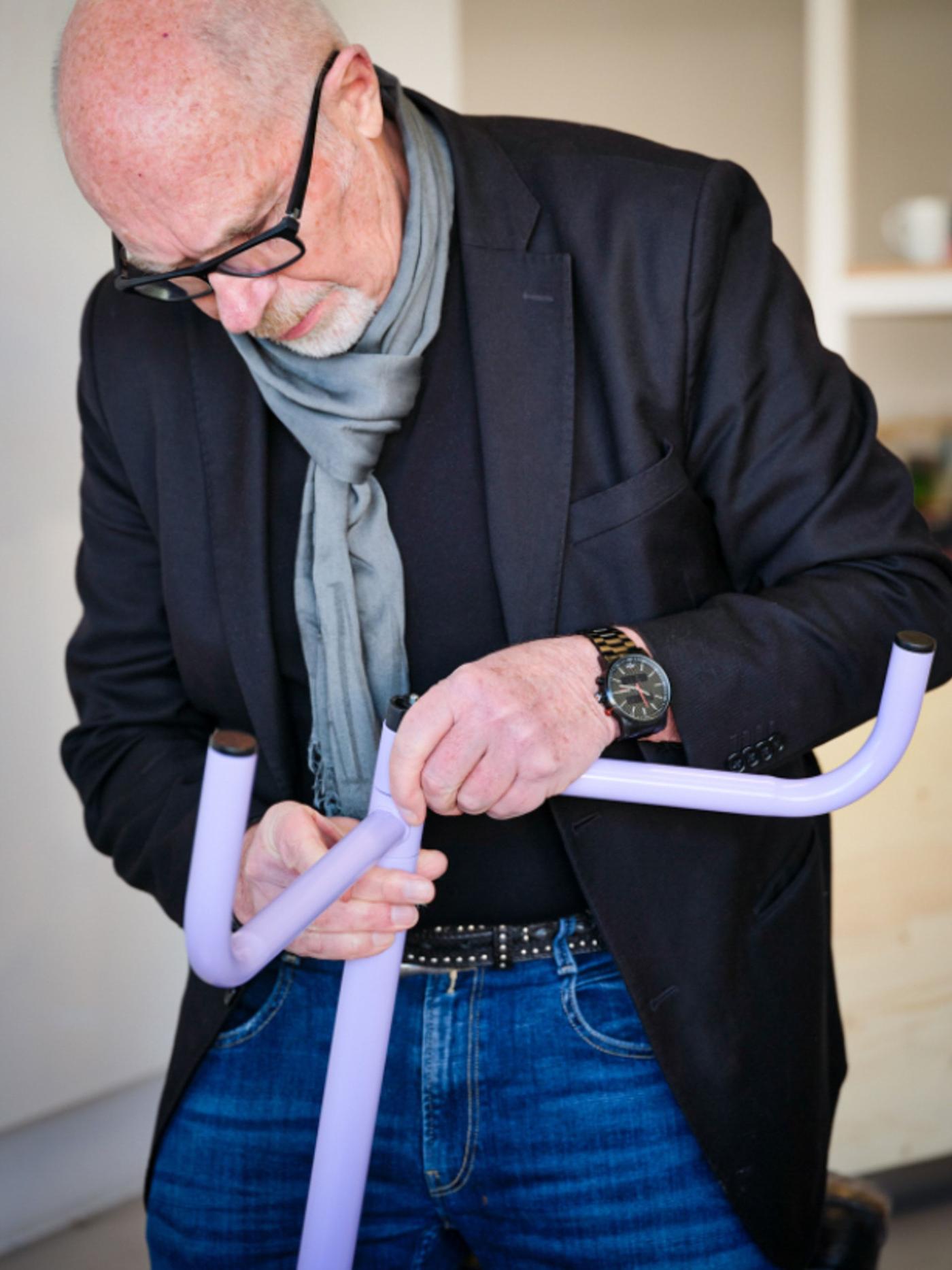 A man in a black jacket and a grey scarf assembling a purple coat hanger.