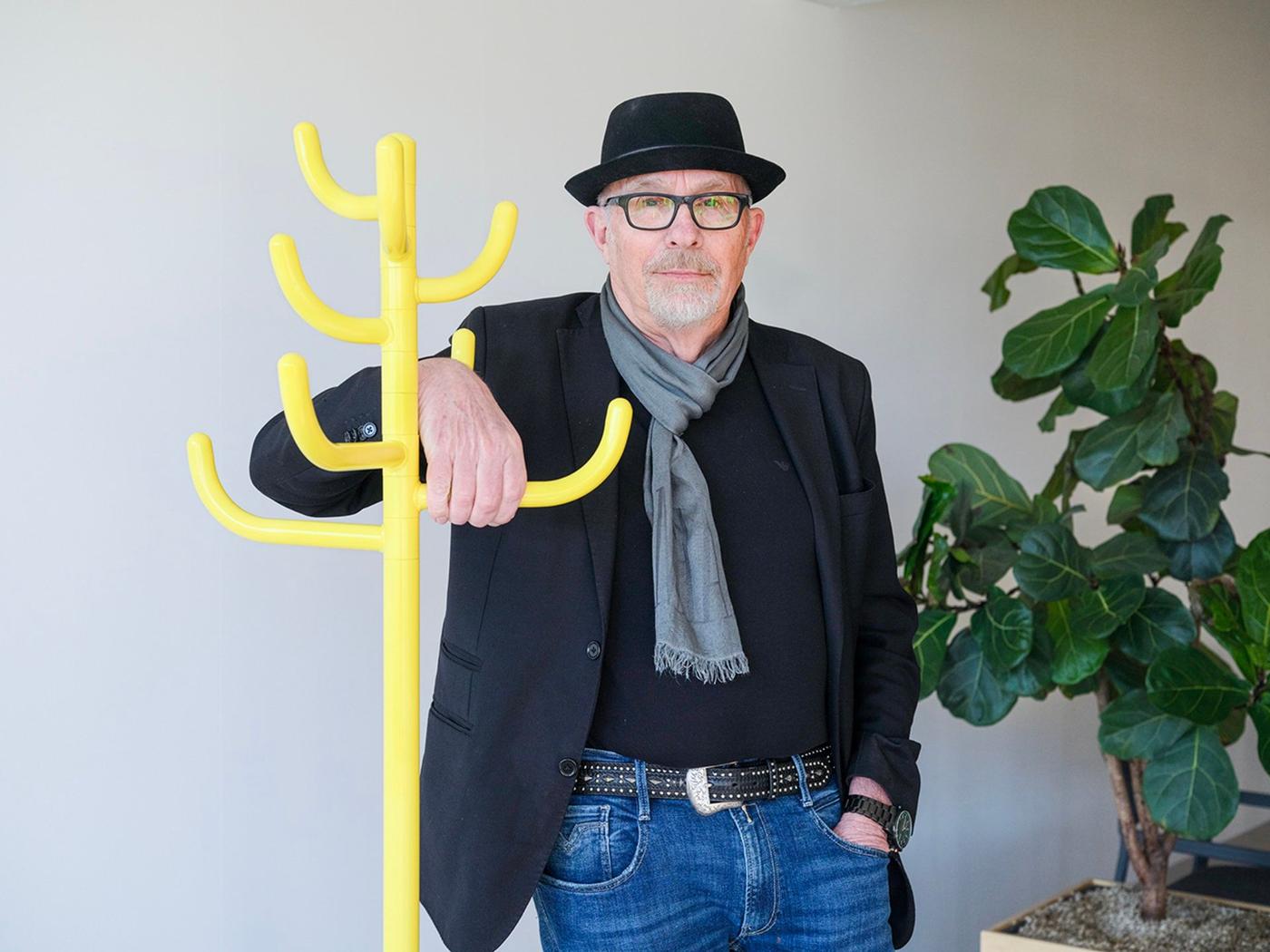 A man in a black jacket and hat standing by a yellow coat hanger.