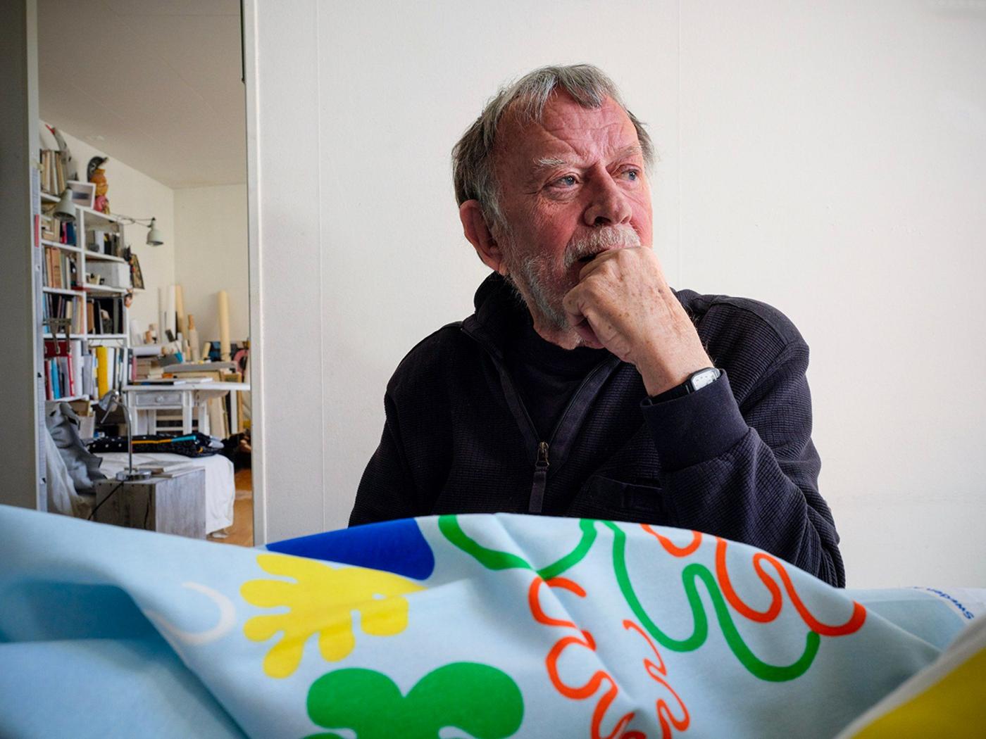 A man looking to the right. In front of him is a table with a colourful fabric.