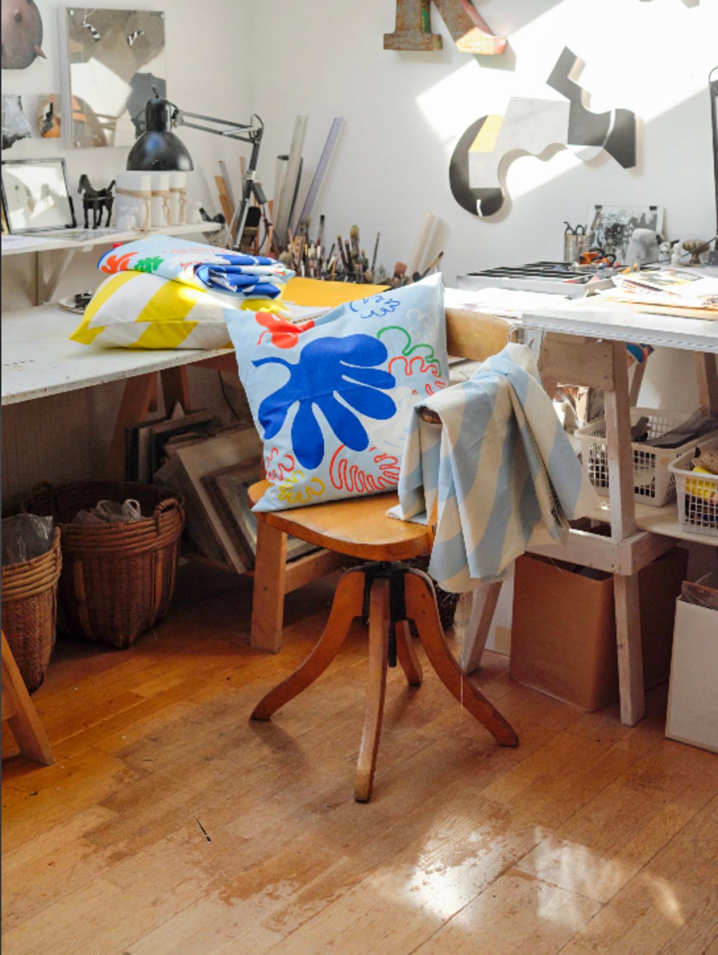 In a room, two pillows and a piece of colourful fabric is placed on a chair.