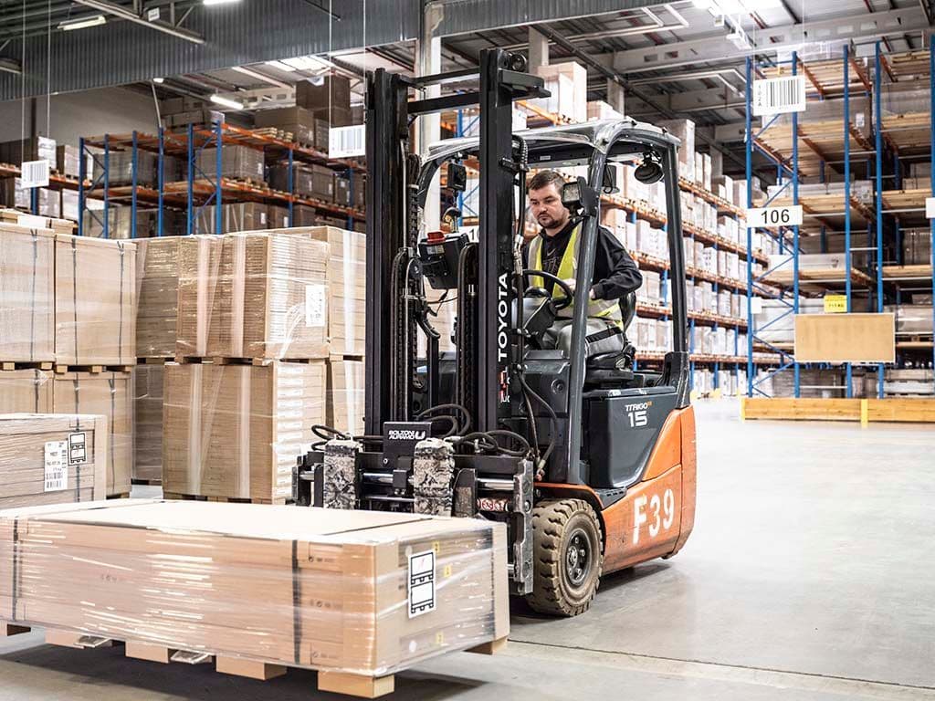 A man drives a forklift truck. He is picking up packages.