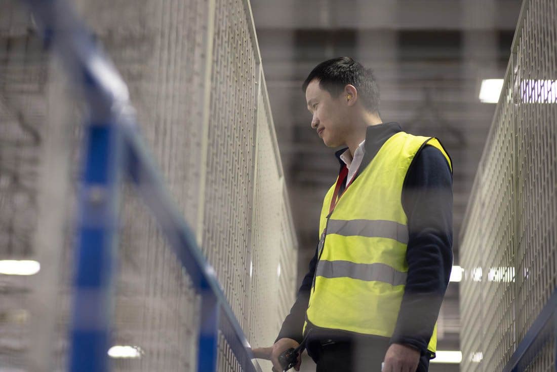 Low-angle view of a co-worker inside an industrial location wearing a fluorescent safety vest.