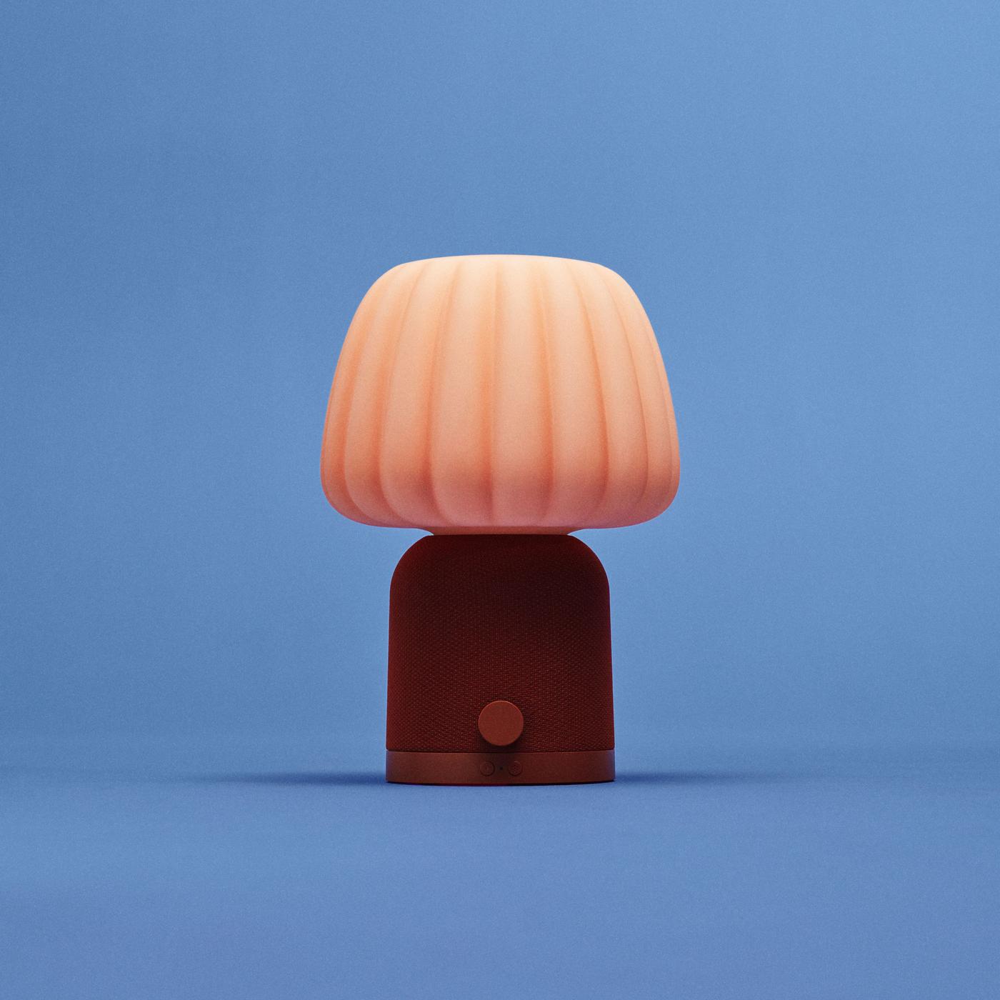 KULGLASS speaker with brown mesh-textured base, red buttons and peach-toned patterned shade, shaped like a table lamp, set against a blue background.