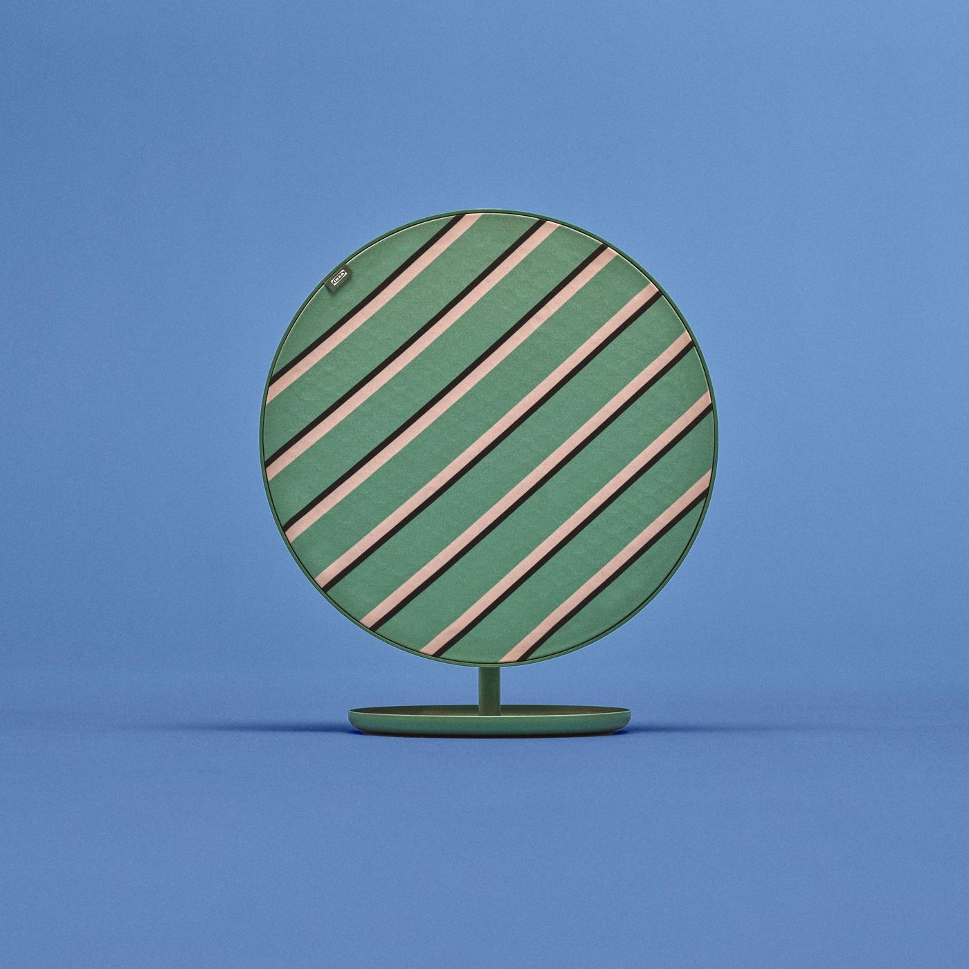 Medium-sized round SOLSKYDD speaker with green, beige, and black cross-stripe pattern on matching green stand, set against a blue background.
