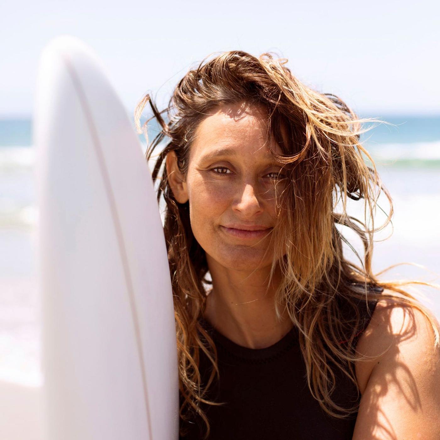 A portrait of a woman on a beach holding a surf board.