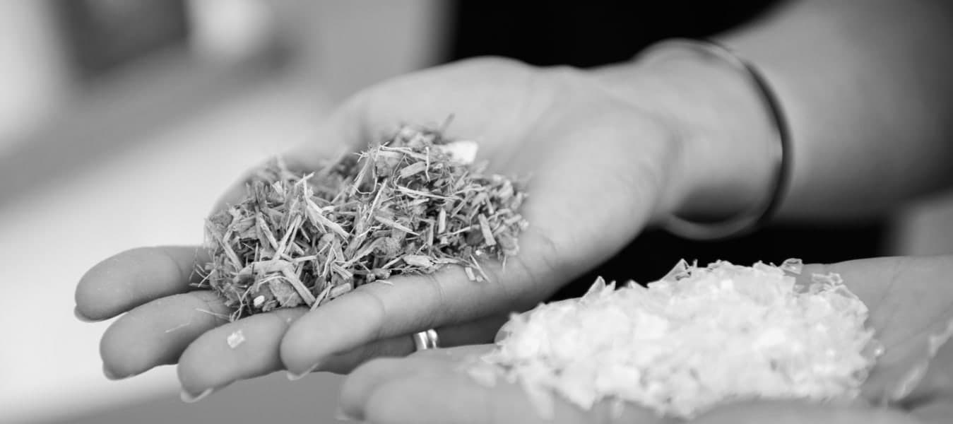 A pair of hands, one holding woodchips and one holding PET plastic chips.