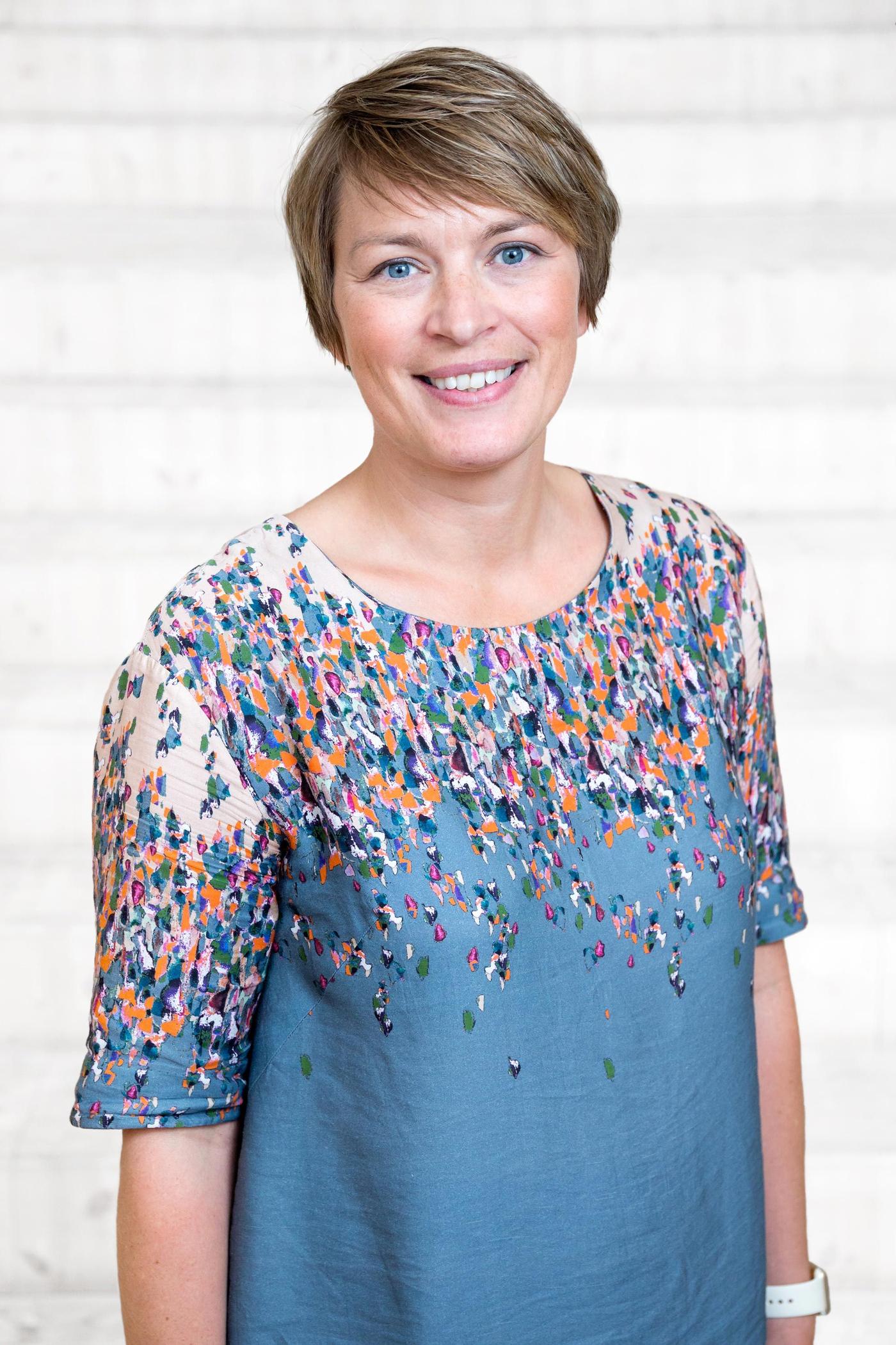 A portrait of a smiling woman wearing a blue top with a colourful pattern.