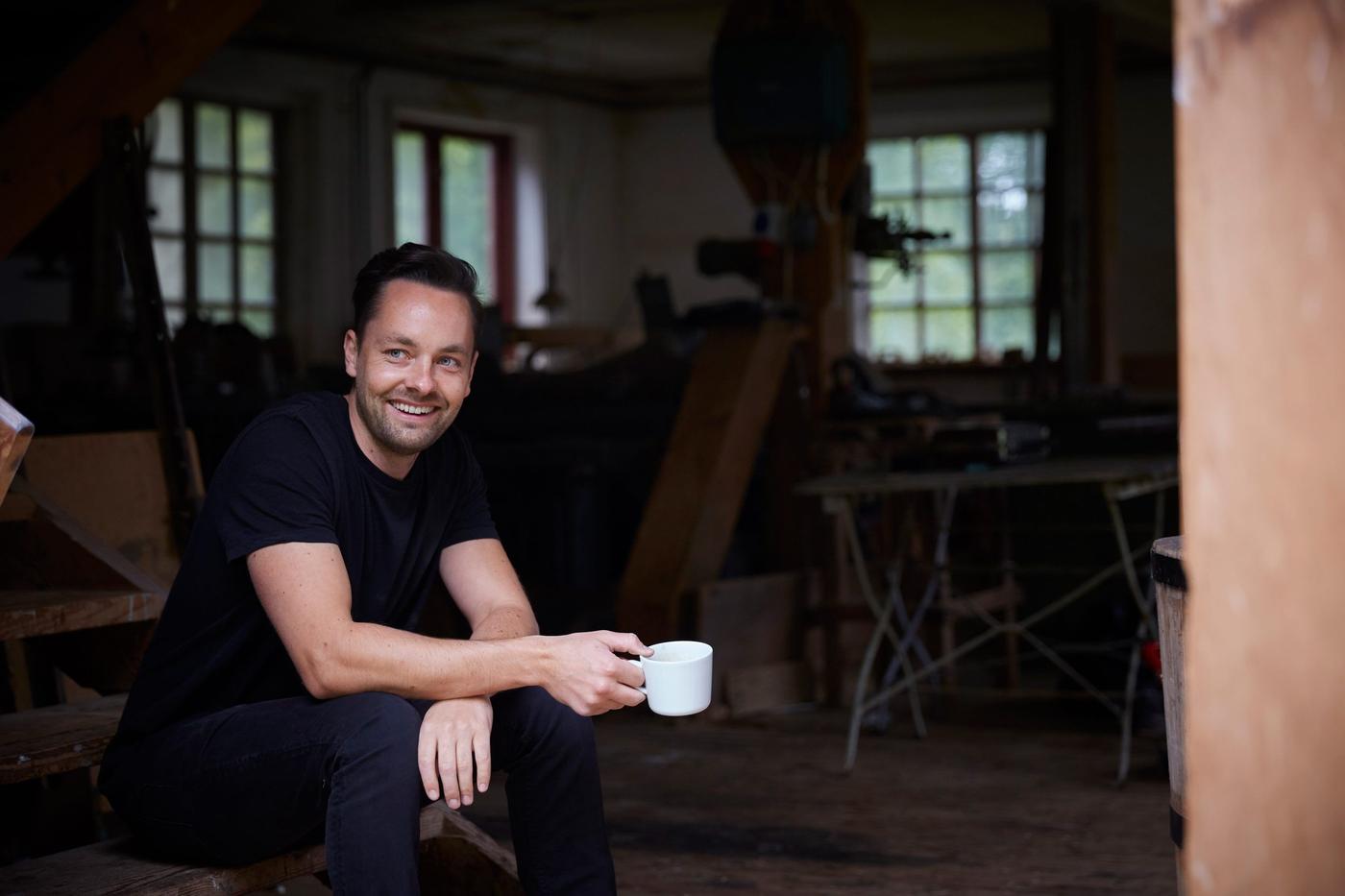 Man holding coffee mug sitting on porch, smiling.