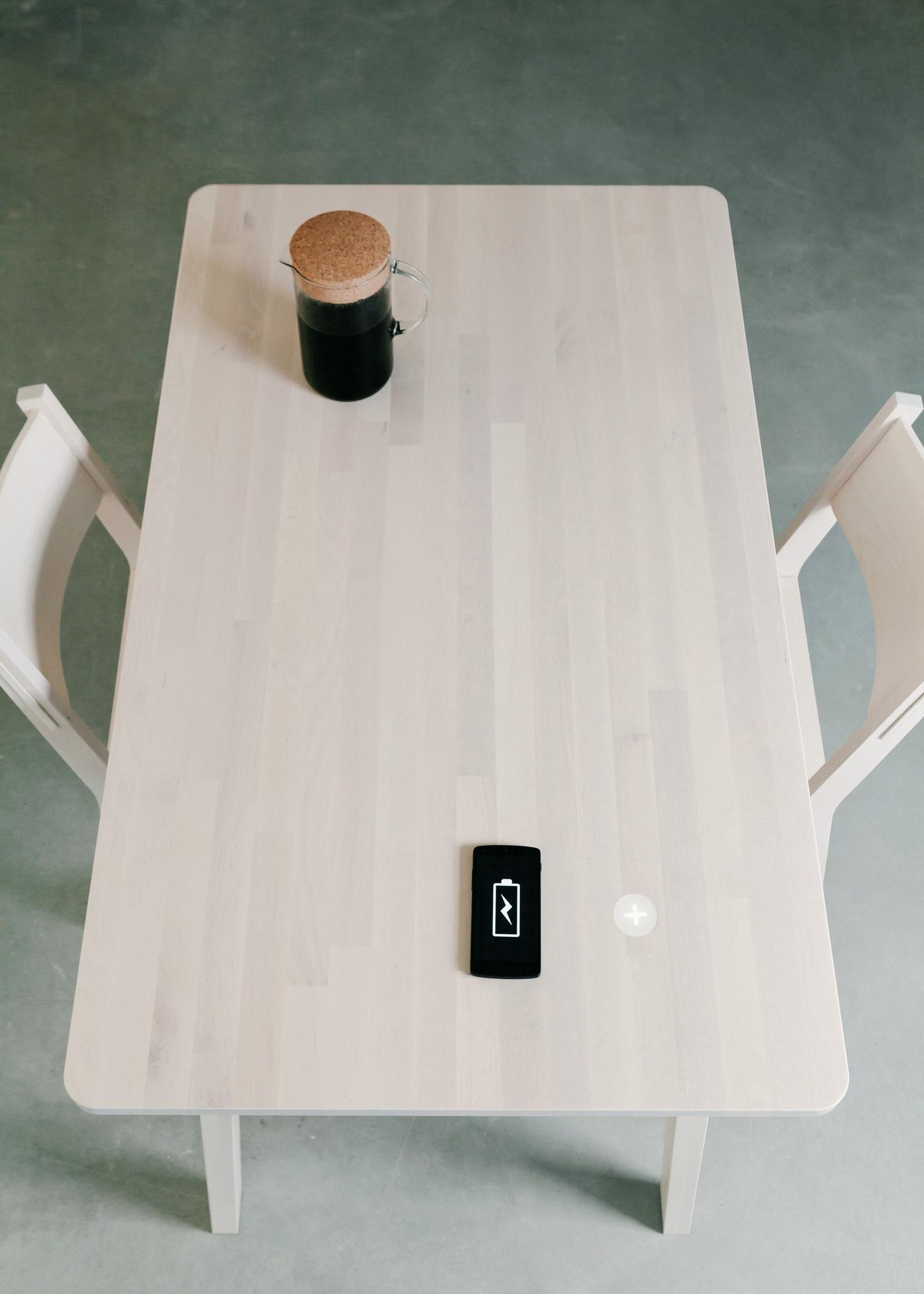 A table and two chairs with a smartphone, and a jug full of coffee.