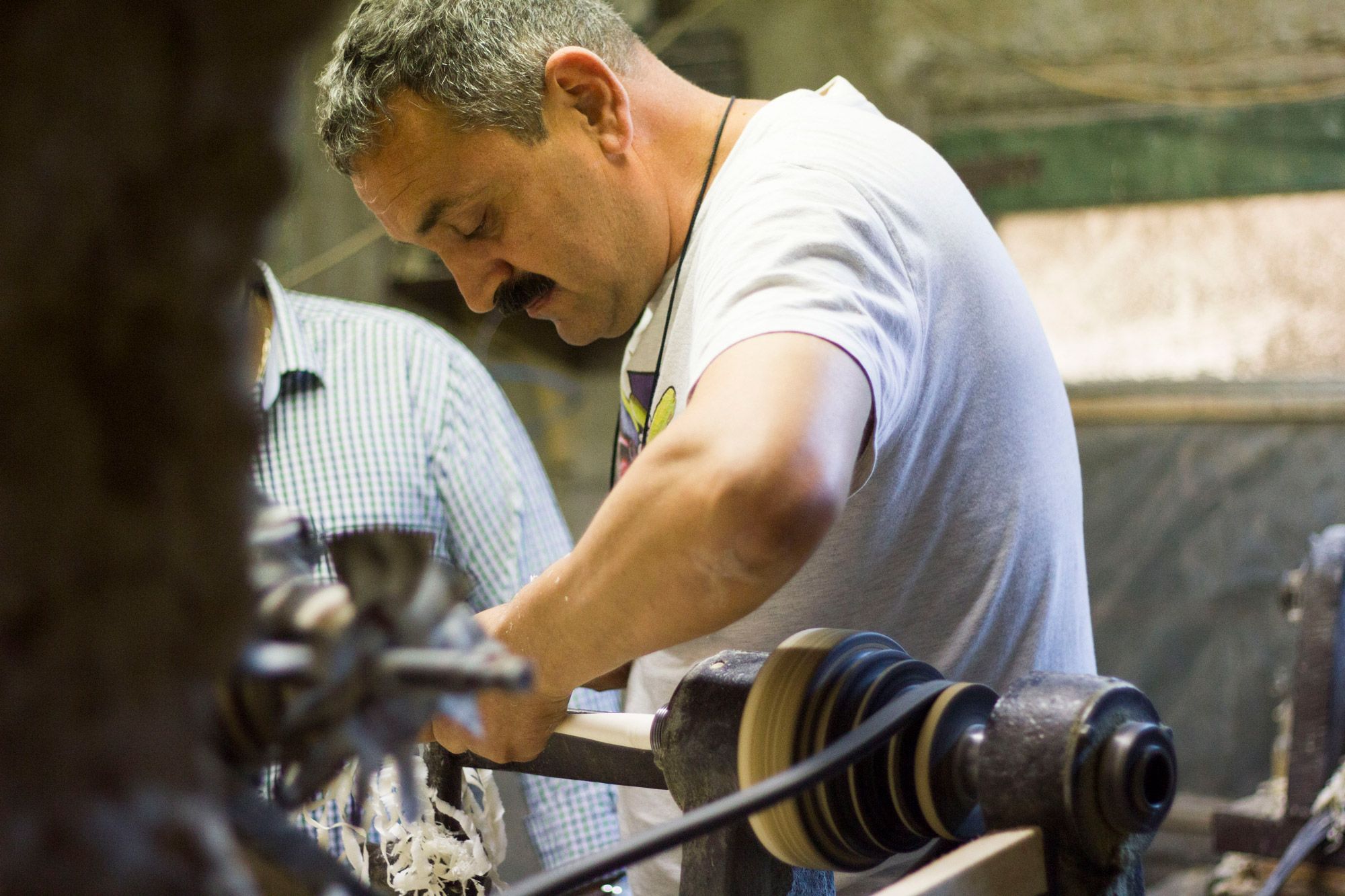 A man in a moustache works a lathe.
