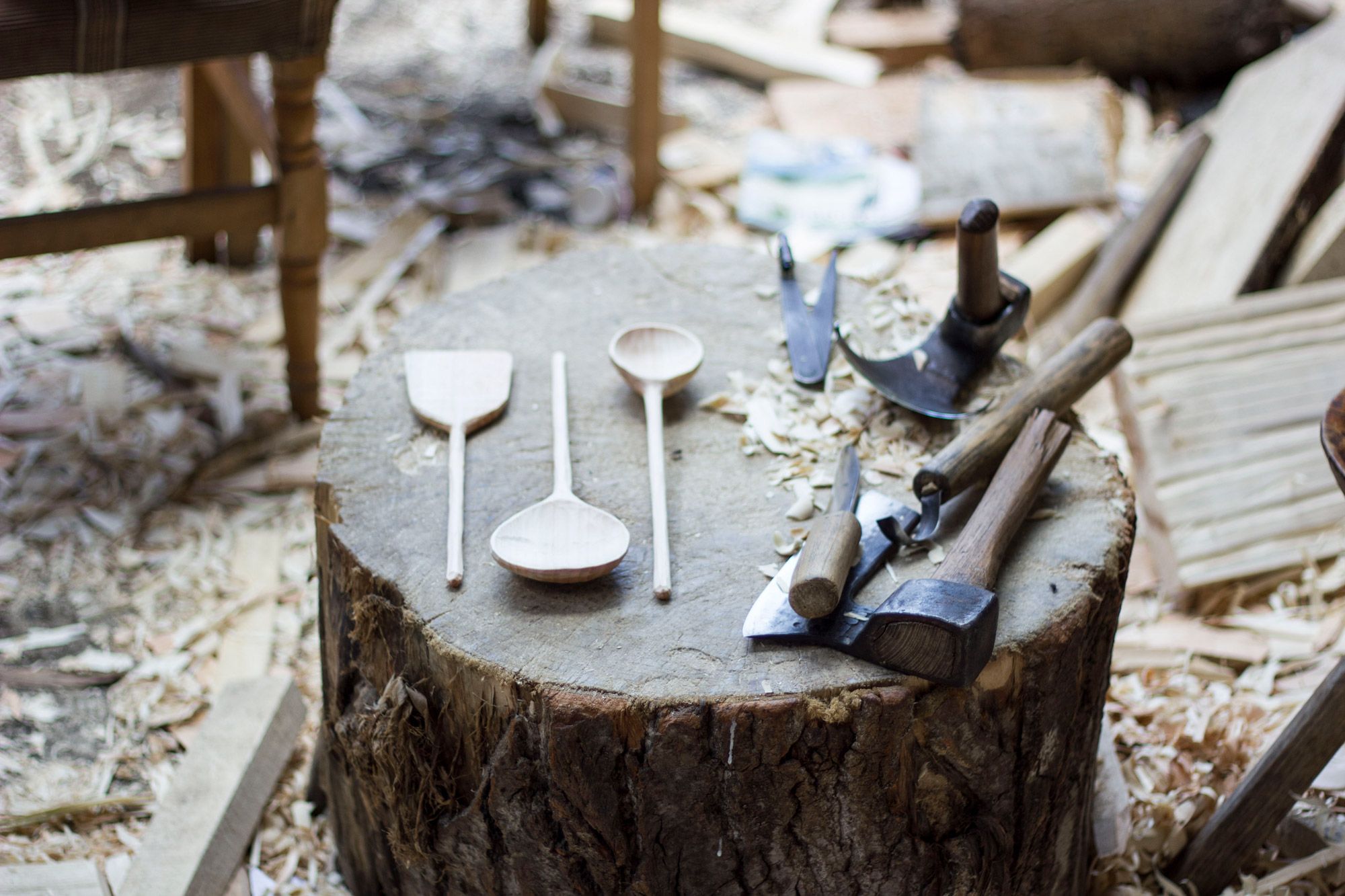 Hand-carved wooden objects and carving tools on a stump, surrounded by wood shavings.
