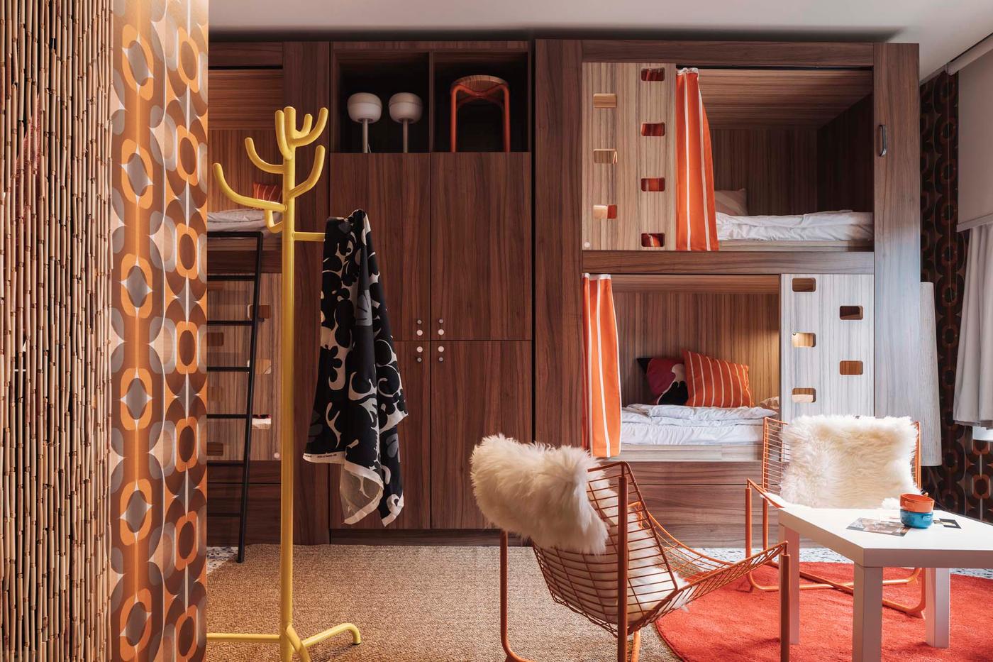 A retro-inspired room with bunk beds built into a wood-panelled wall and an orange SKÅLBODA armchair in the foreground.