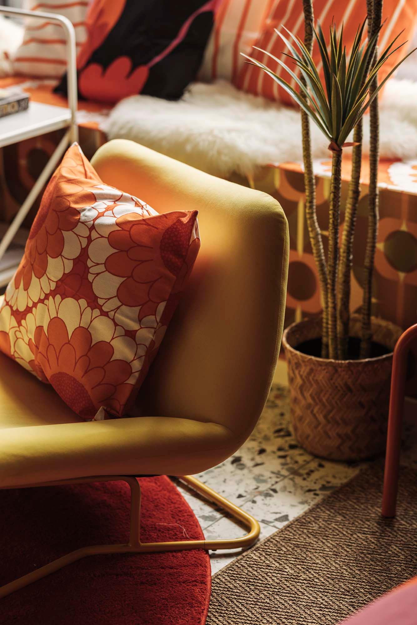 A pot plant behind a hakebo yellow SOTENÄS armchair with a cushion in a SANDETERNELL cushion cover.