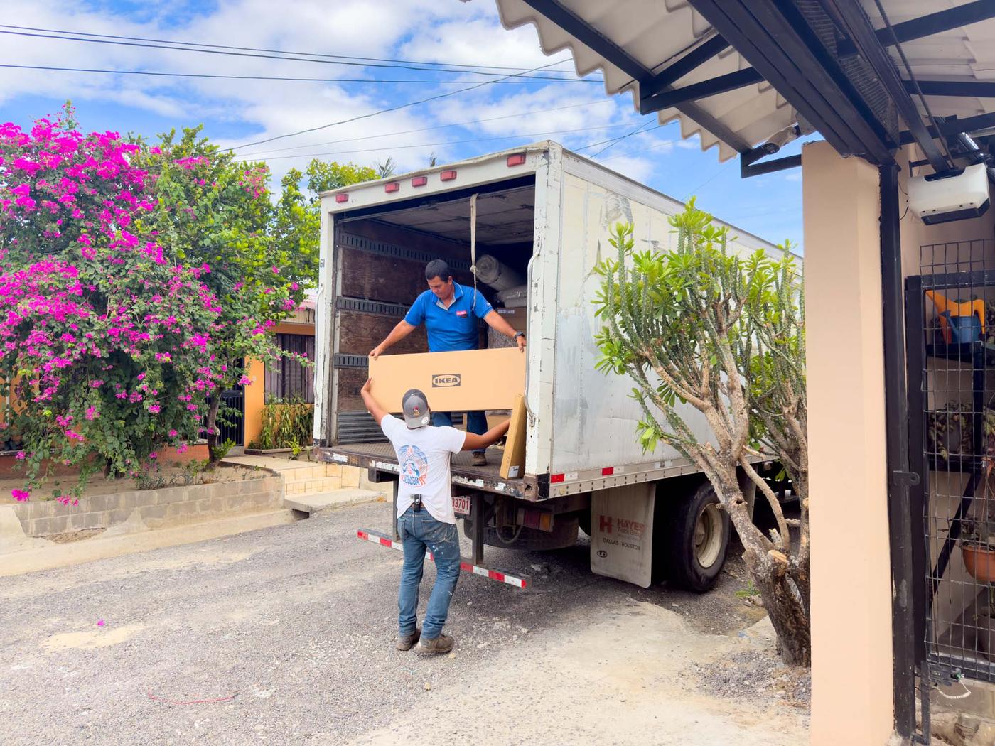 A person in the back of a lorry hands a long IKEA flatpack box down to his colleague in the street.
