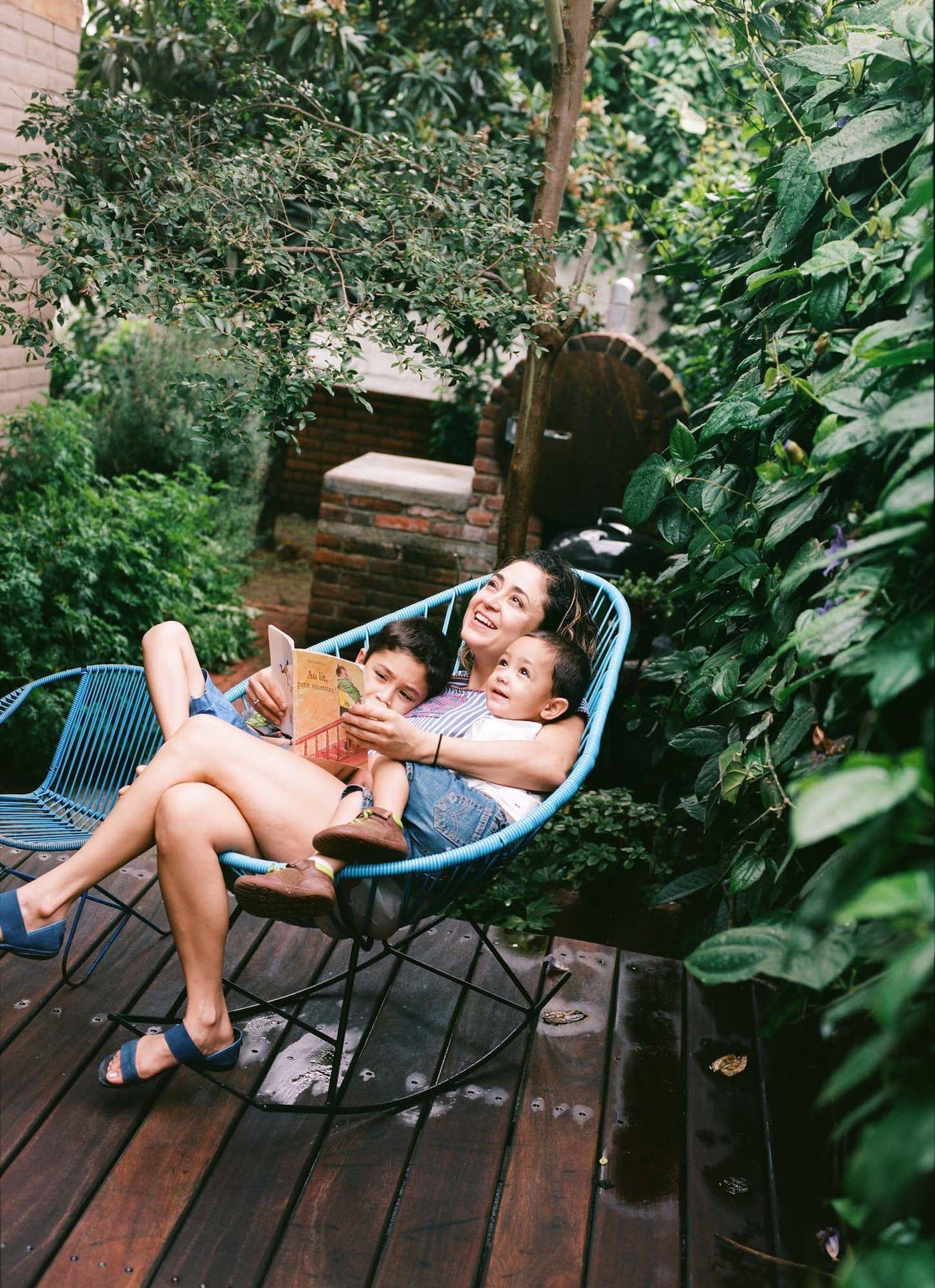 A parent reads a book outside on a terrace with two small children.