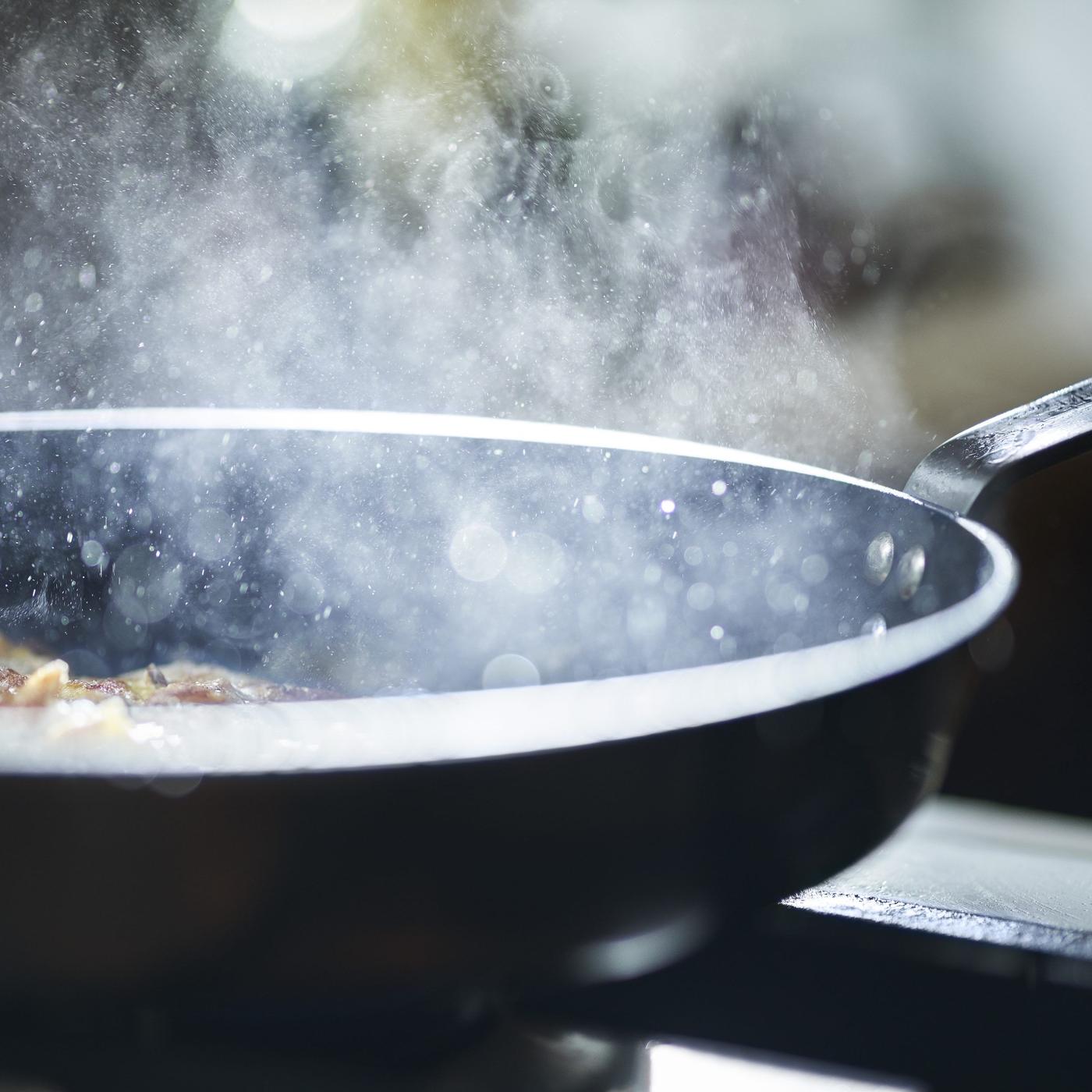 A frying pan with smoke coming out of it while frying food.