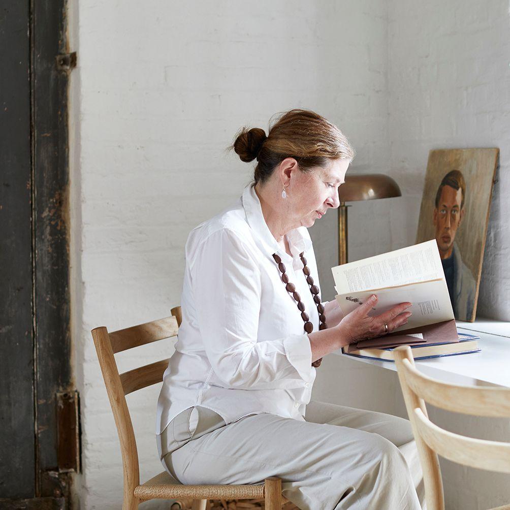 Ilse Crawford seated at a table reading a book.