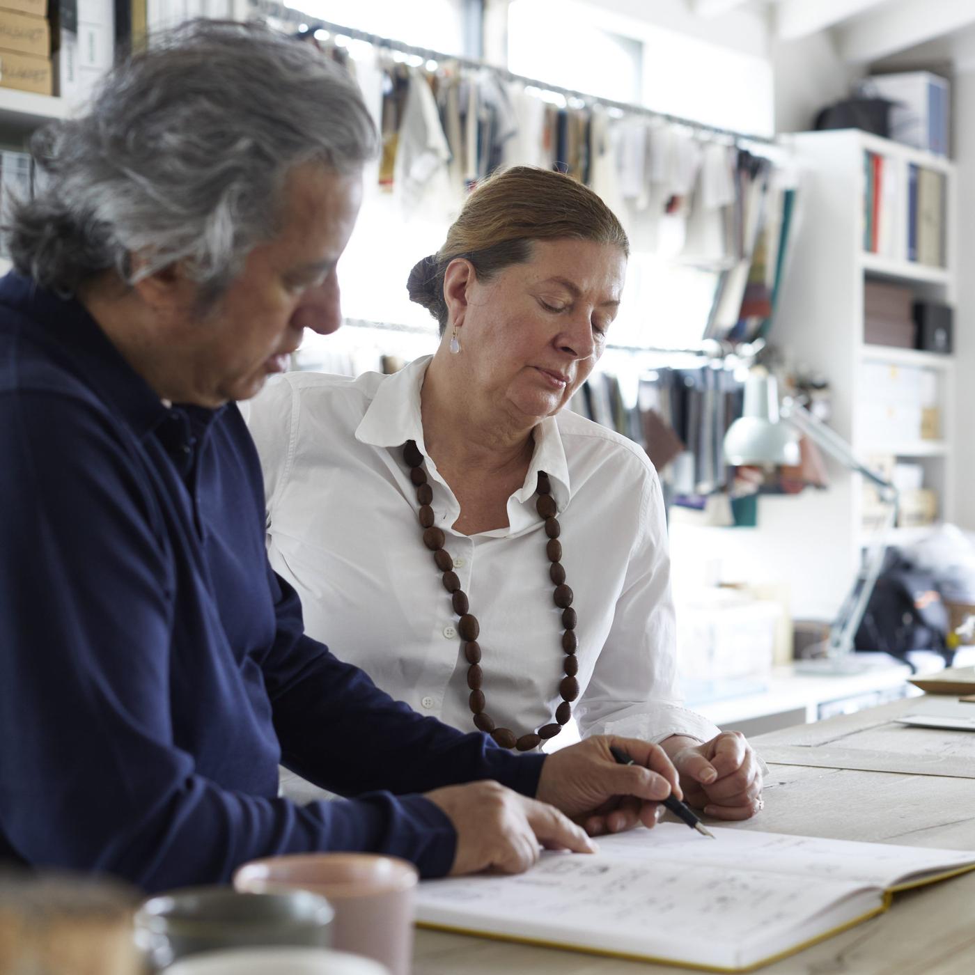 Ilse Crawford and Oscar Peña stand at a worktop looking at a book together.