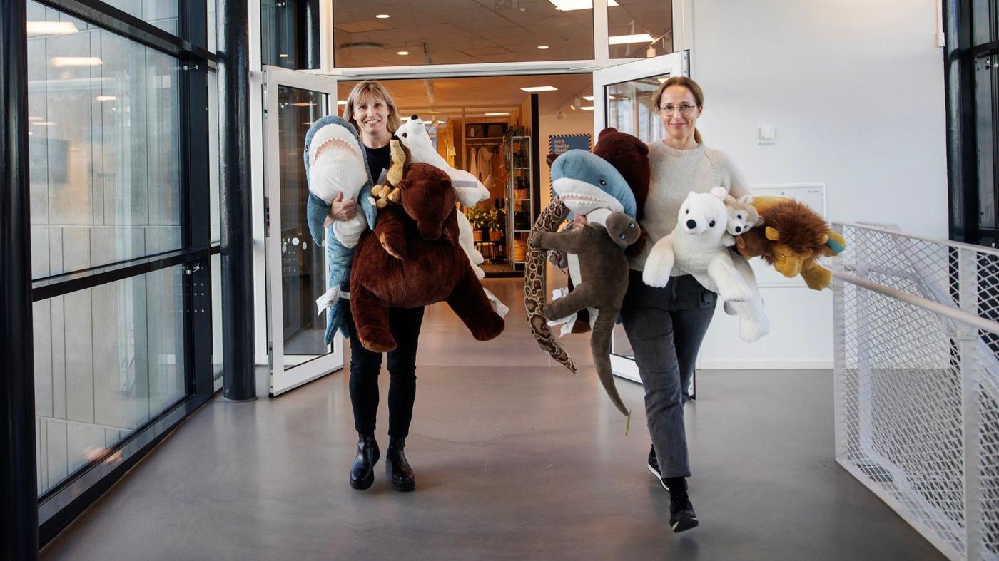 Two women carrying soft toys walking in a hallway.