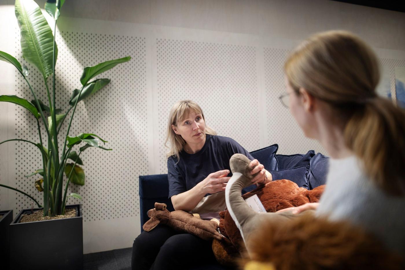 Two women sitting in a sofa, one of them holding a soft toy.
