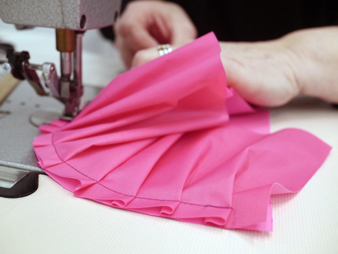 Hands sewing a magenta-coloured fabric.