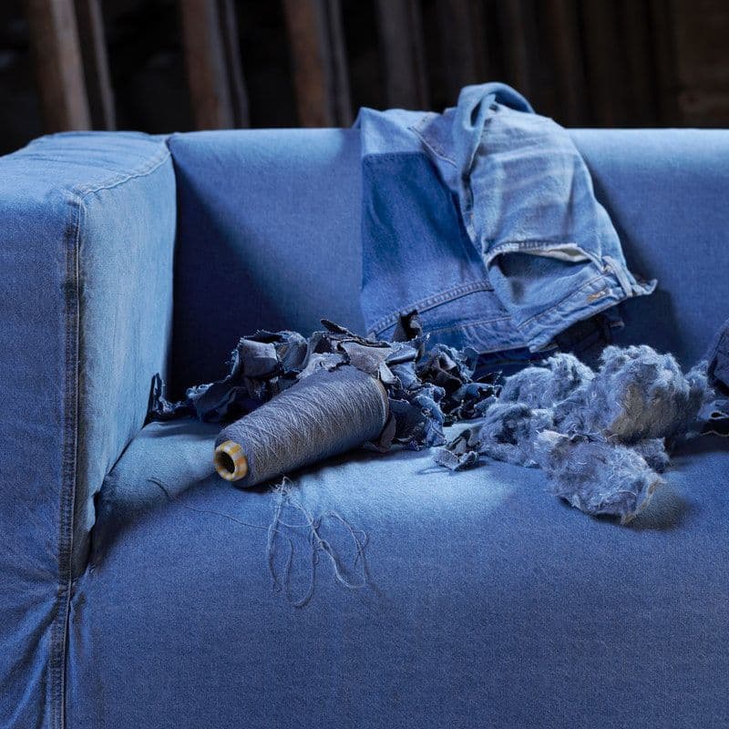 A sofa with a denim cover, with a spool of blue thread, a pair of jeans and balled-up denim cuttings.