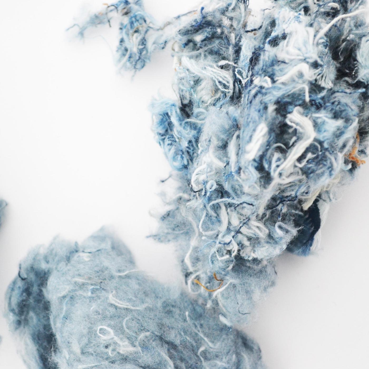 Fluffy balls of shredded denim threads on a white surface.