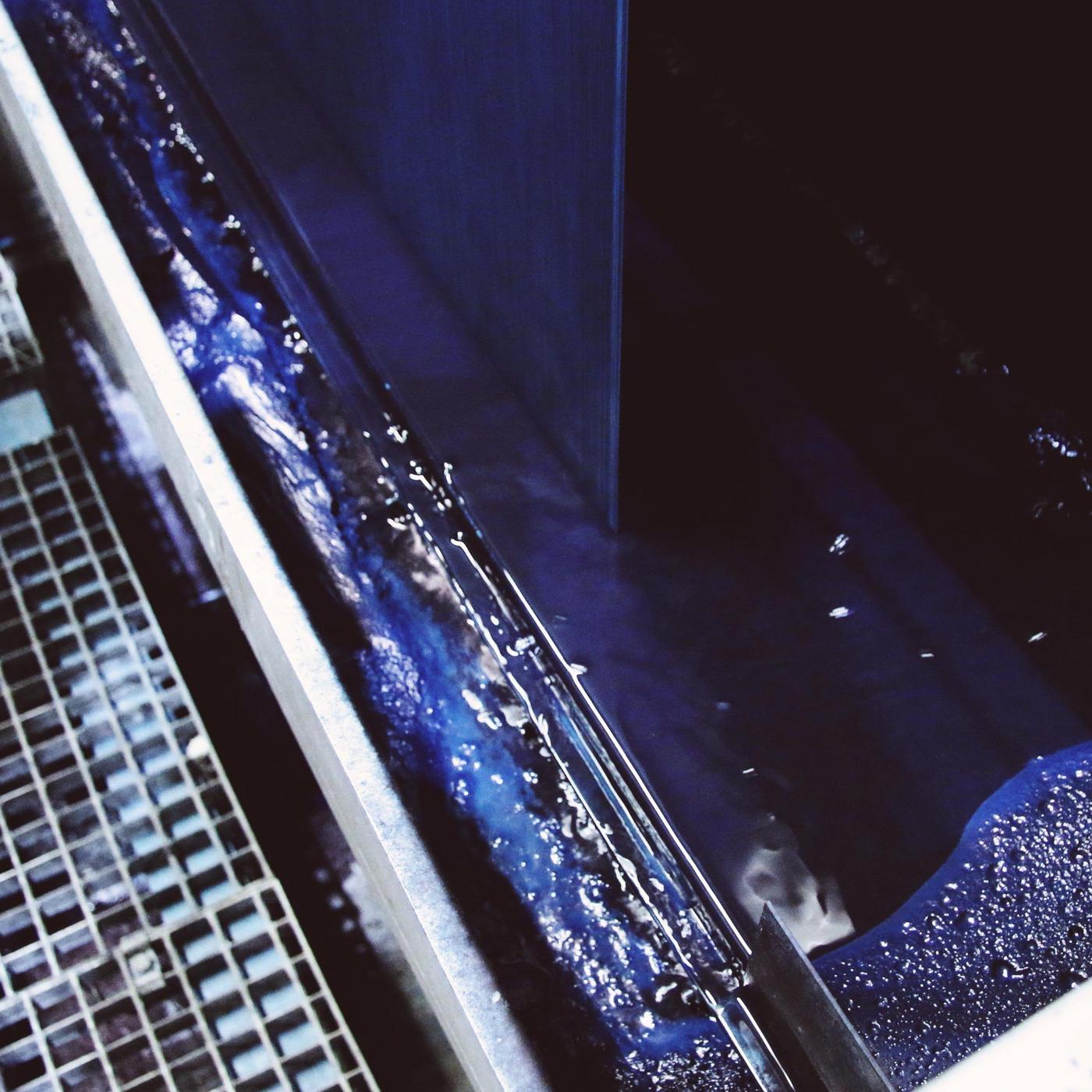 A blue dyeing bath inside a machine, with hundreds of fine threads running into it.