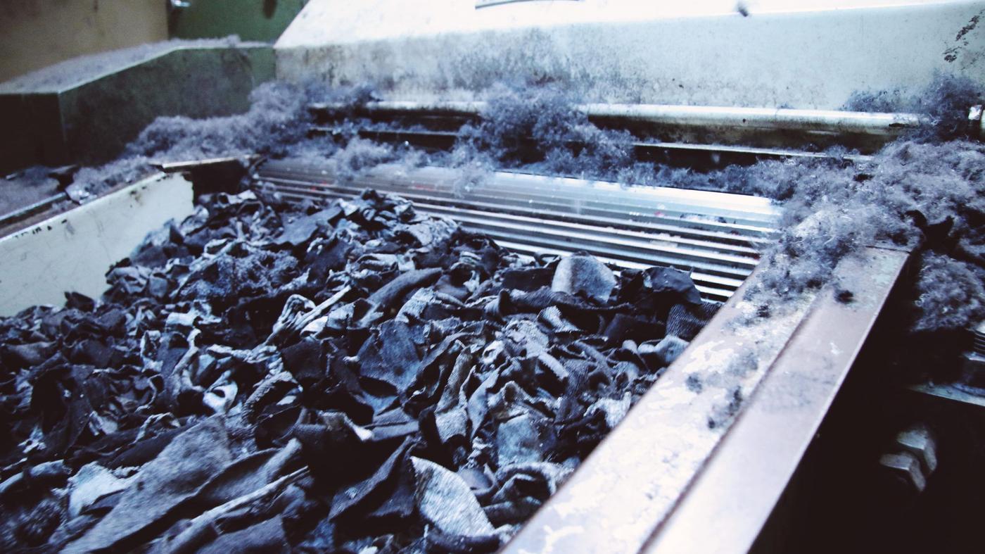 Denim-fabric cuttings being fed into a machine, with thick blue denim dust around the opening.