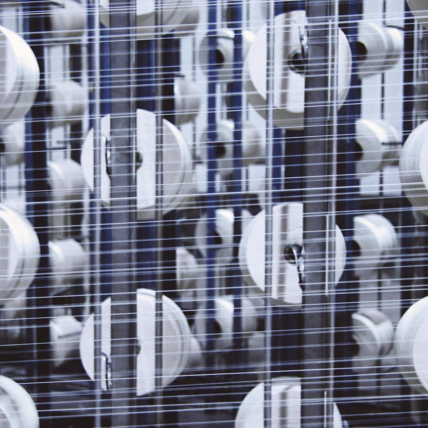 Spools of white thread inside a machine, with the threads running horizontally through it.
