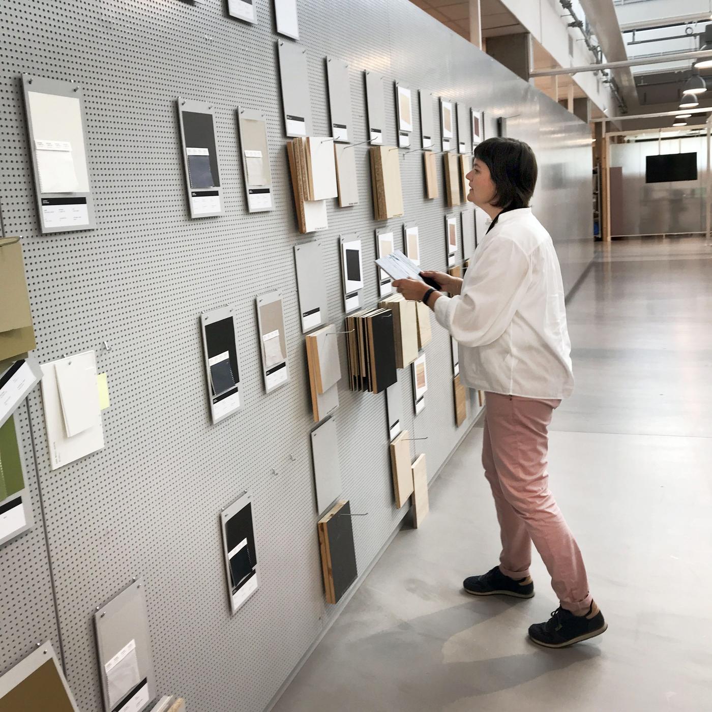 A woman looking at colour samples hanging on a perforated wall.