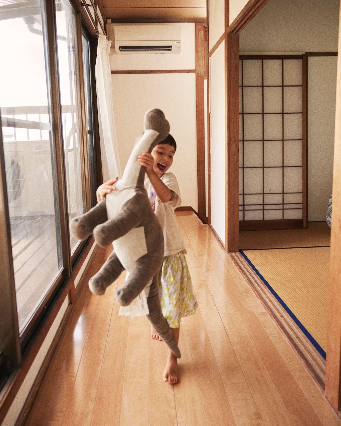 A child playing with a large dinosaur soft toy in a bright hallway with wooden floors.