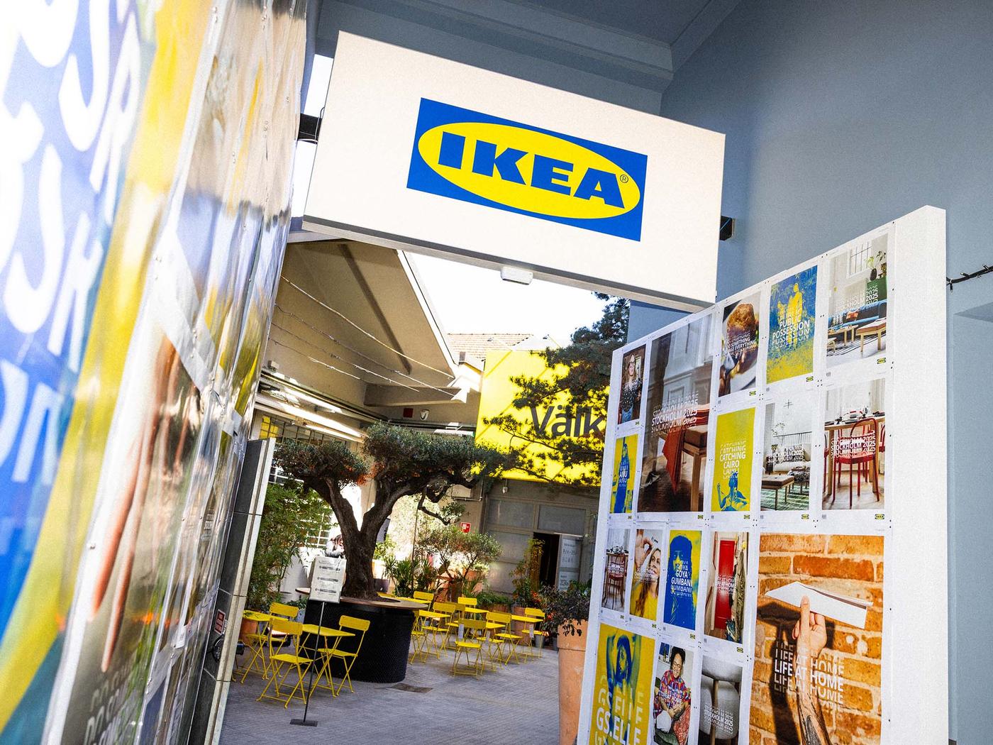 The entrance to the IKEA Milan Design Week exhibition in milan with posters on the wall, and a tree inside the venue.