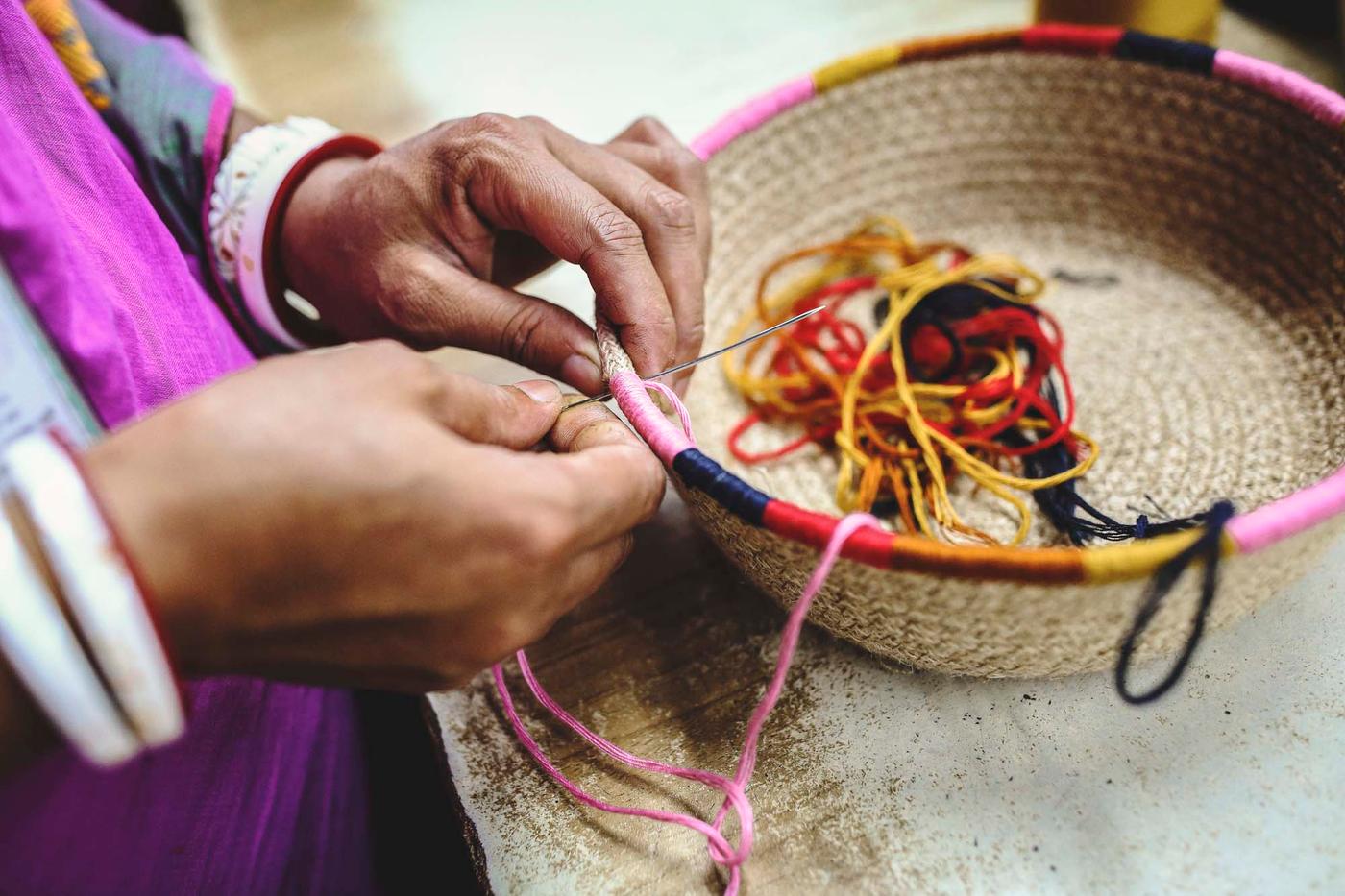 A person is sewing coloured decorative details onto a basket.