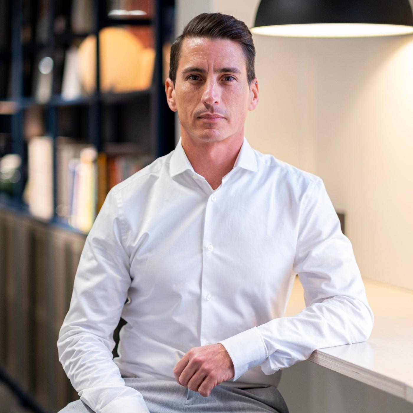 A man in a white shirt sitting on a stool at a desk.