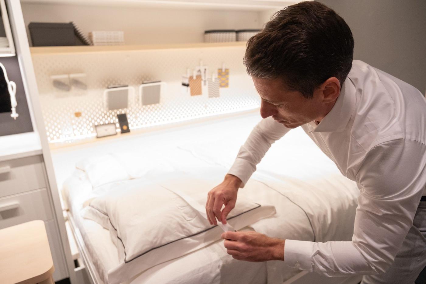 A man standing next to a bed, putting his hands on a pillow.