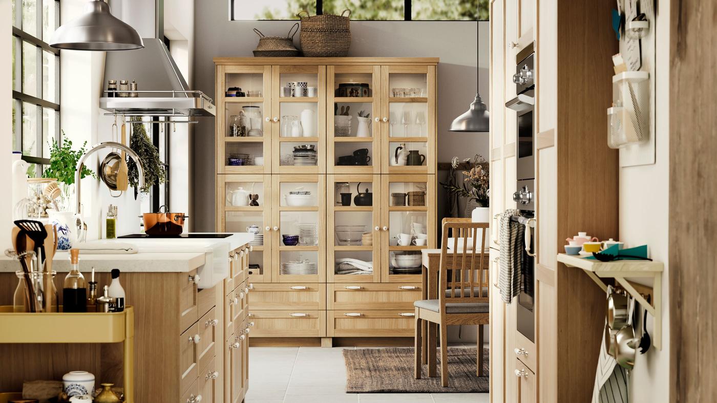 An airy light wood and white METOD kitchen with wood and glass-fronted FORSBACKA doors filled with kitchenware.
