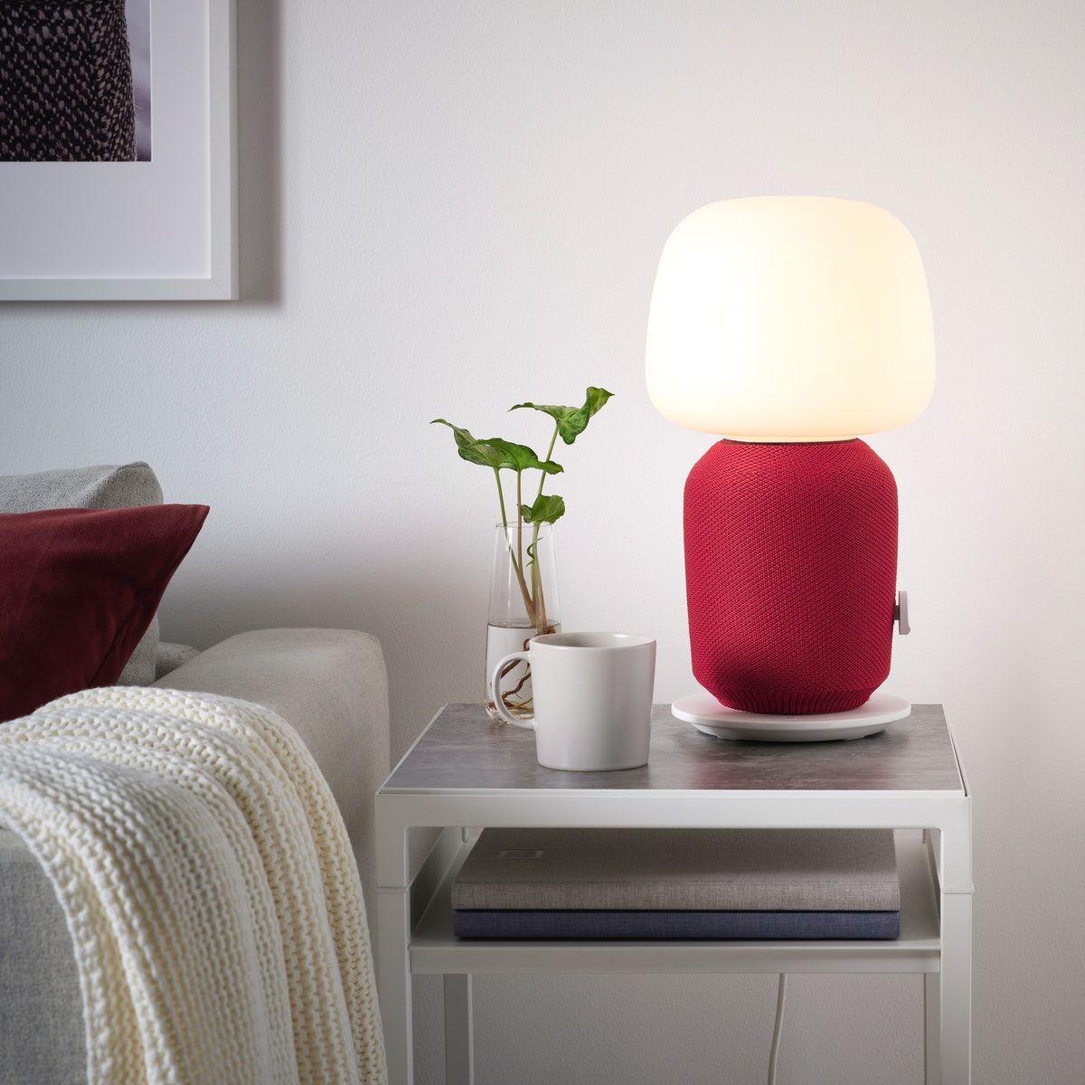 A SYMFONISK table lamp with WiFi speaker standing on a table beside a sofa.