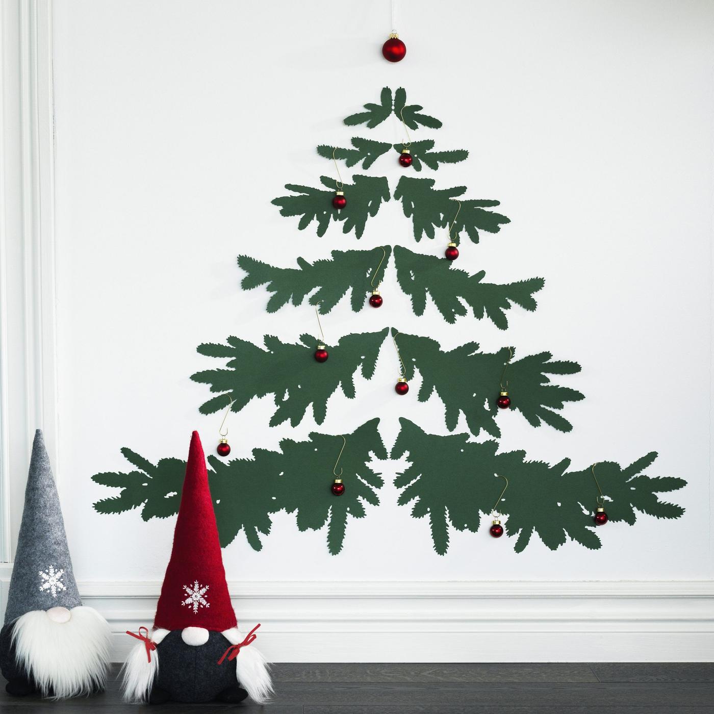 Two elflike Christmas decorations and branches of a Christmas tree painted on a wall with red baubles.