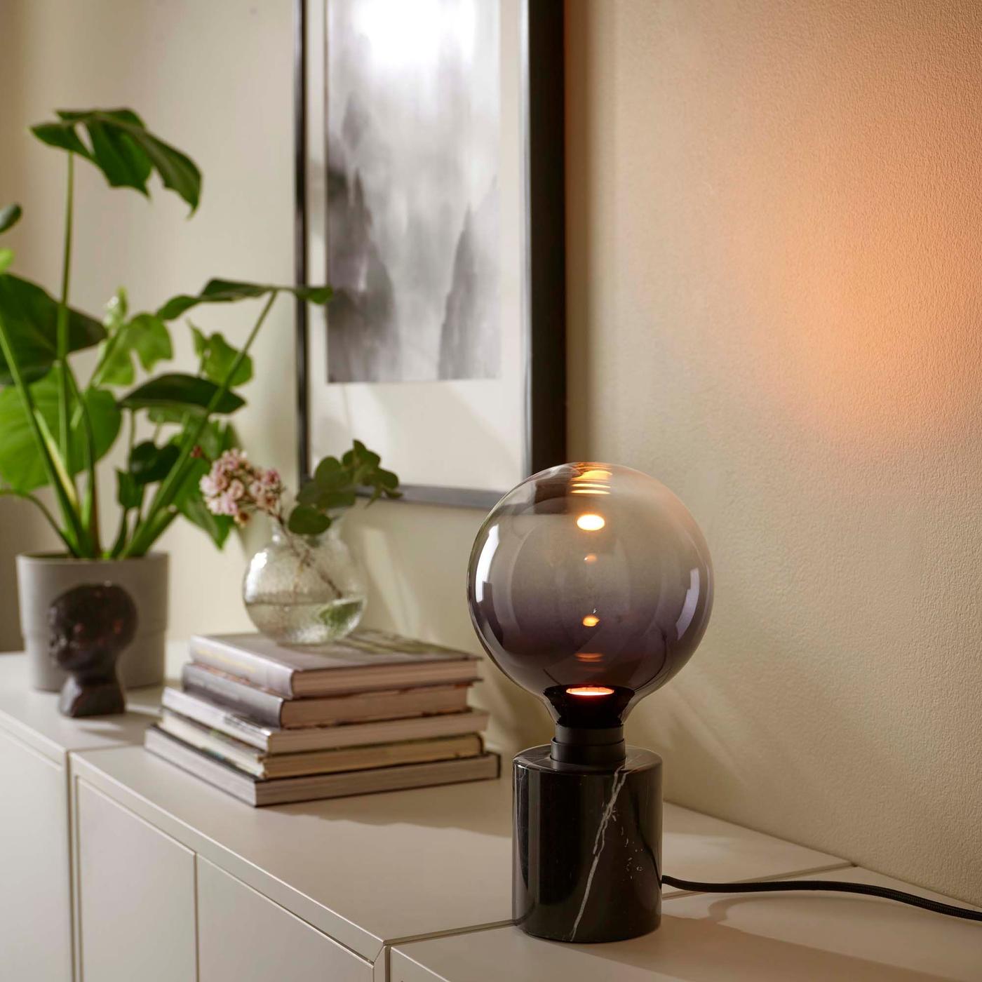 A black marble table lamp with a large dark and light grey bulb on a light beige side table.