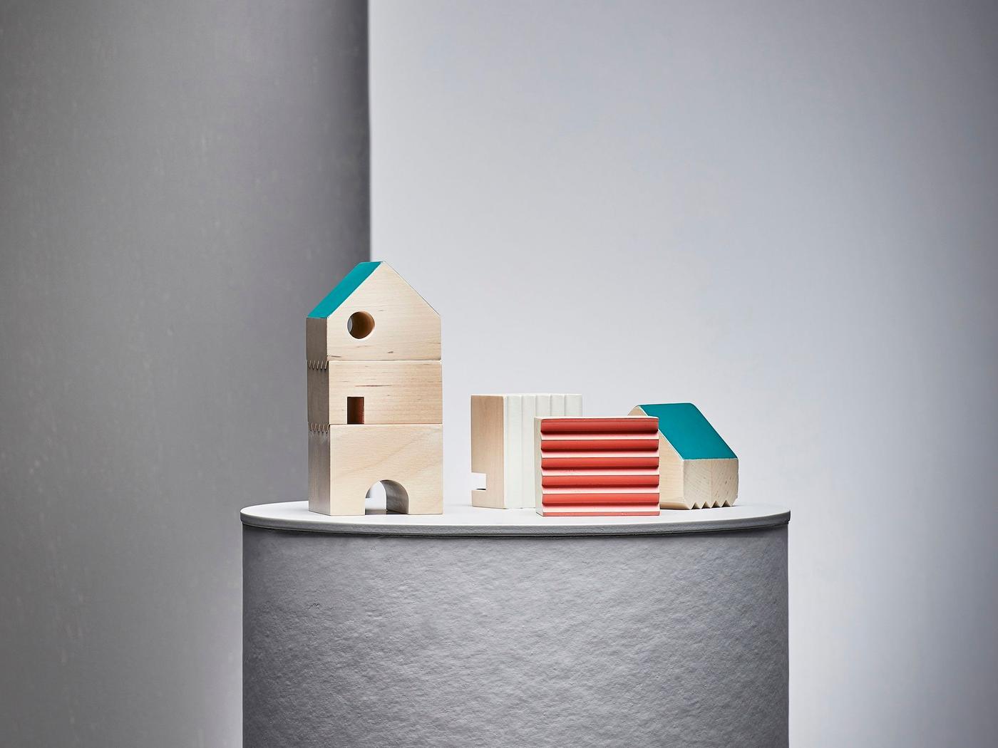 A set of 3 FÄLTLÖNN decoration houses, made from solid wood, displayed on a white pedestal in a white studio space.