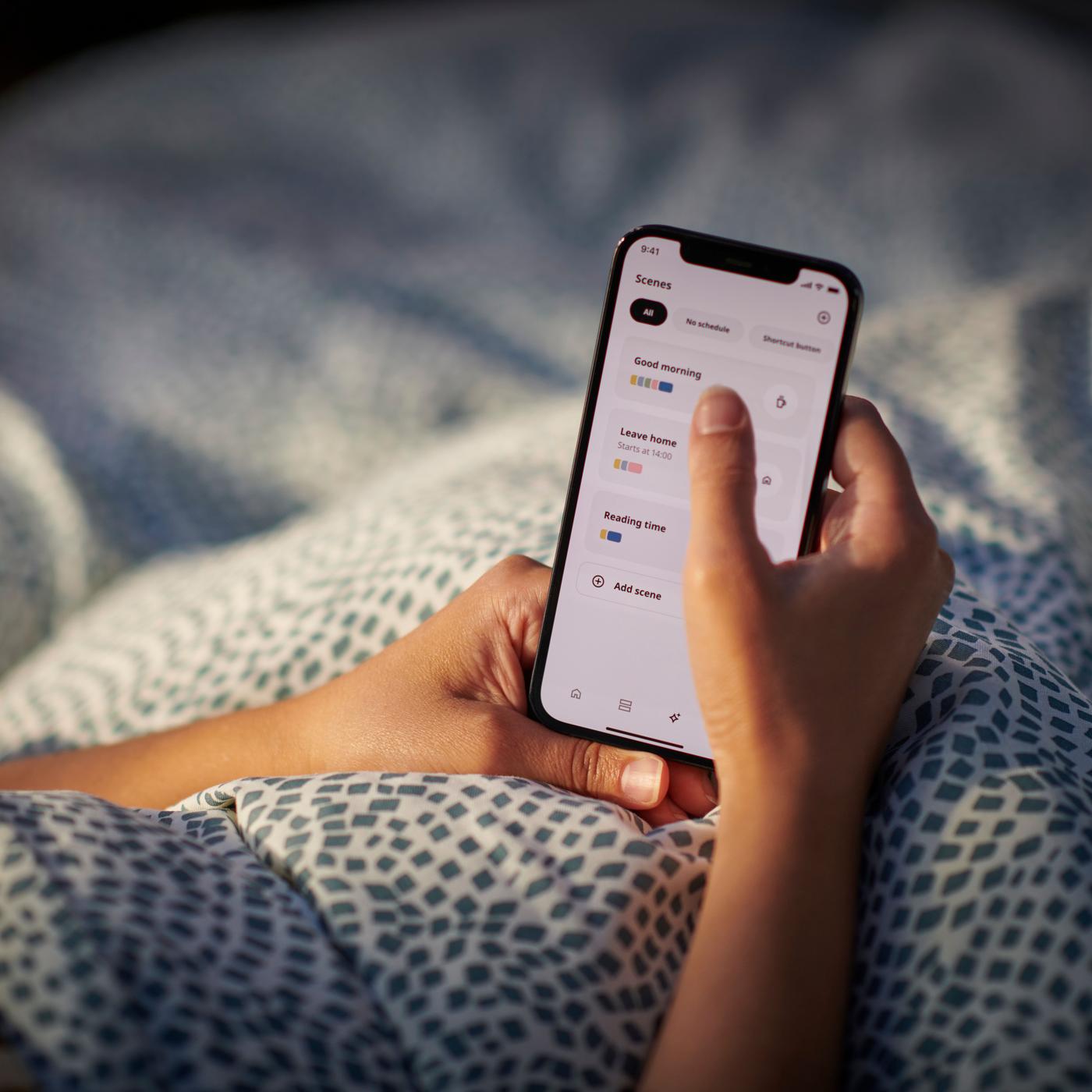 Two hands are holding a phone that is displaying the IKEA Home smart app.