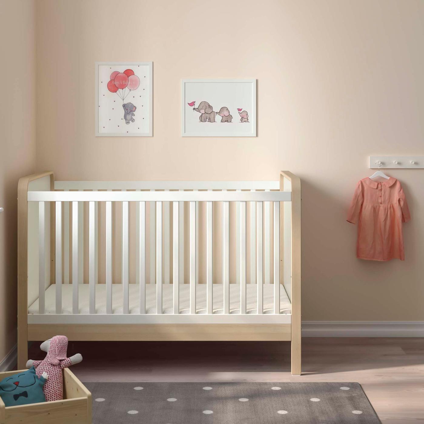 A cot in a pale pink room with a grey rug in front and two framed pictures on the wall above.