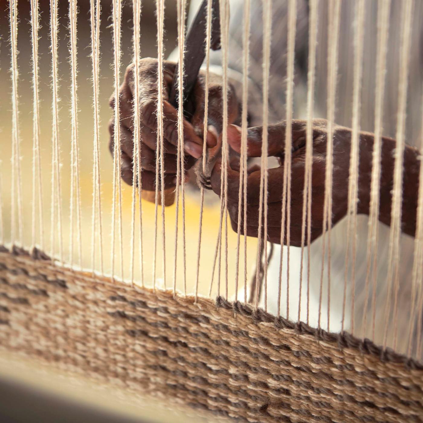 A pair of hands threading wool onto a loom, to make a rug.
