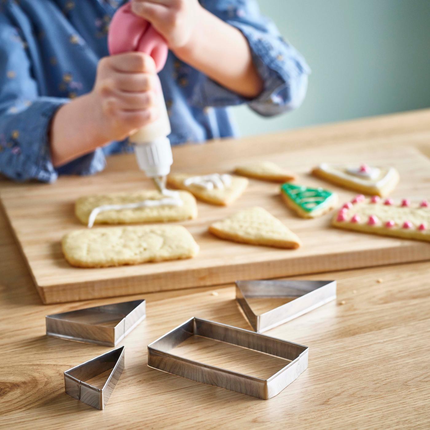 A close-up of a child decorating homemade biscuits that have been cut into shapes using cookie cutters.