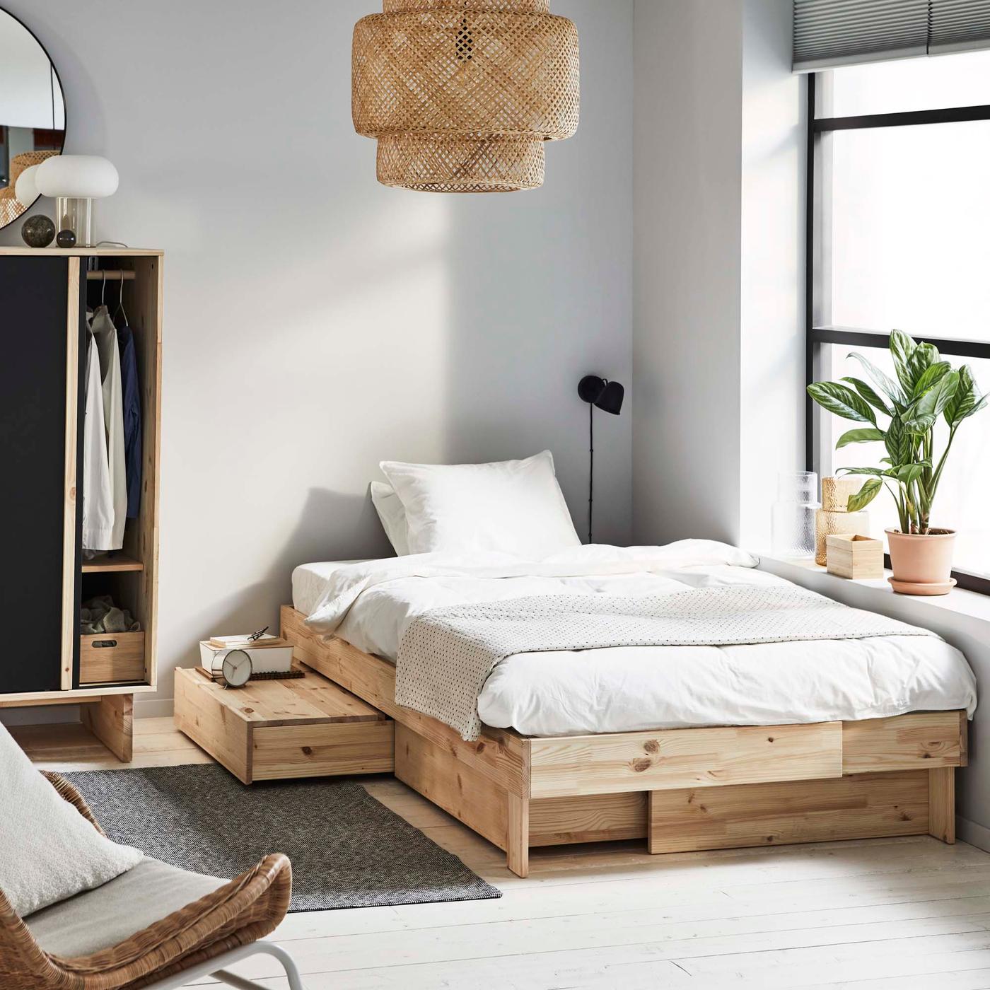 A wooden GLAMBERGET bed in a room, next to a window.