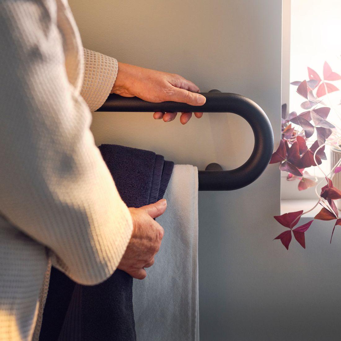 A person holding the BÄSINGEN towel rail with one hand while grabbing a towel with the other hand.