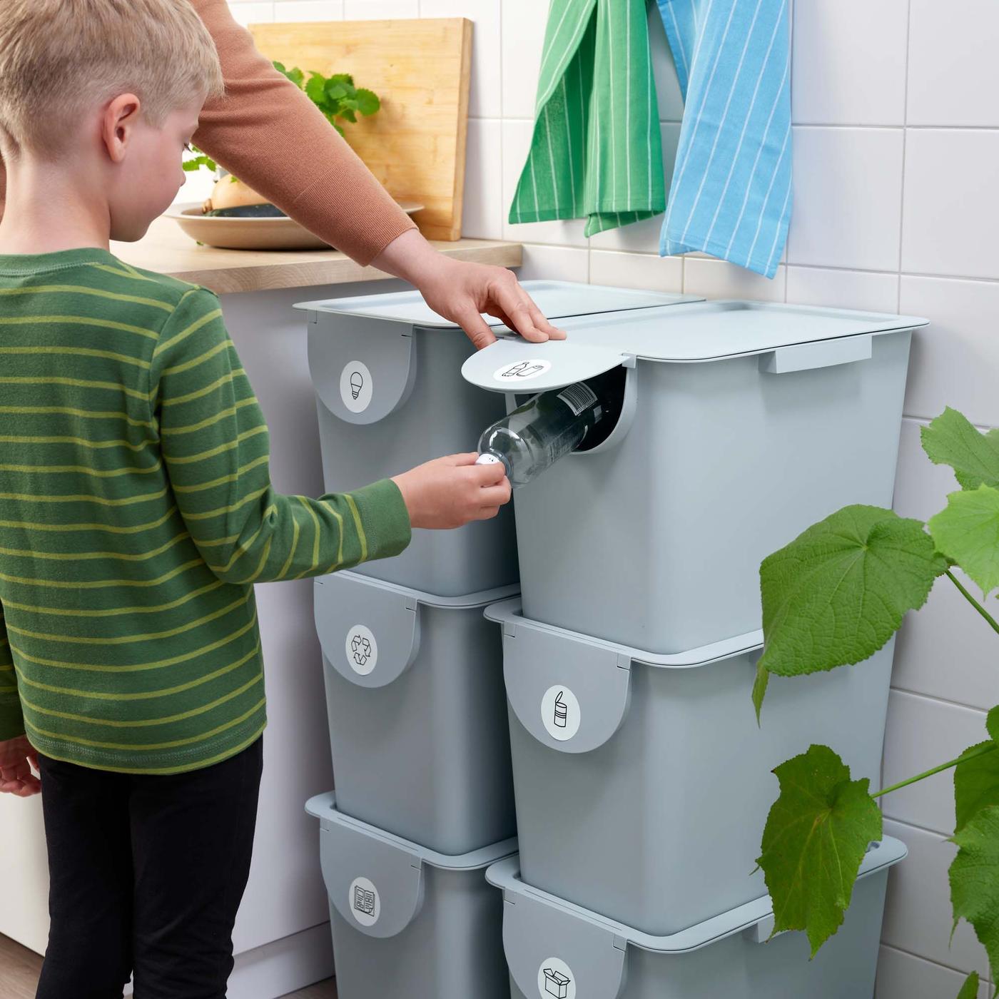 A child puts an object into the opening of one of a stack of recycling containers.